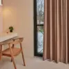 Bora dim-out curtain fabric in a warm brown tone, made from 90% polyester and 10% linen, shown as floor-length curtains in a modern interior, soft textured drapery with light-filtering properties, OEKOTEX certified and suitable for Roman blinds.