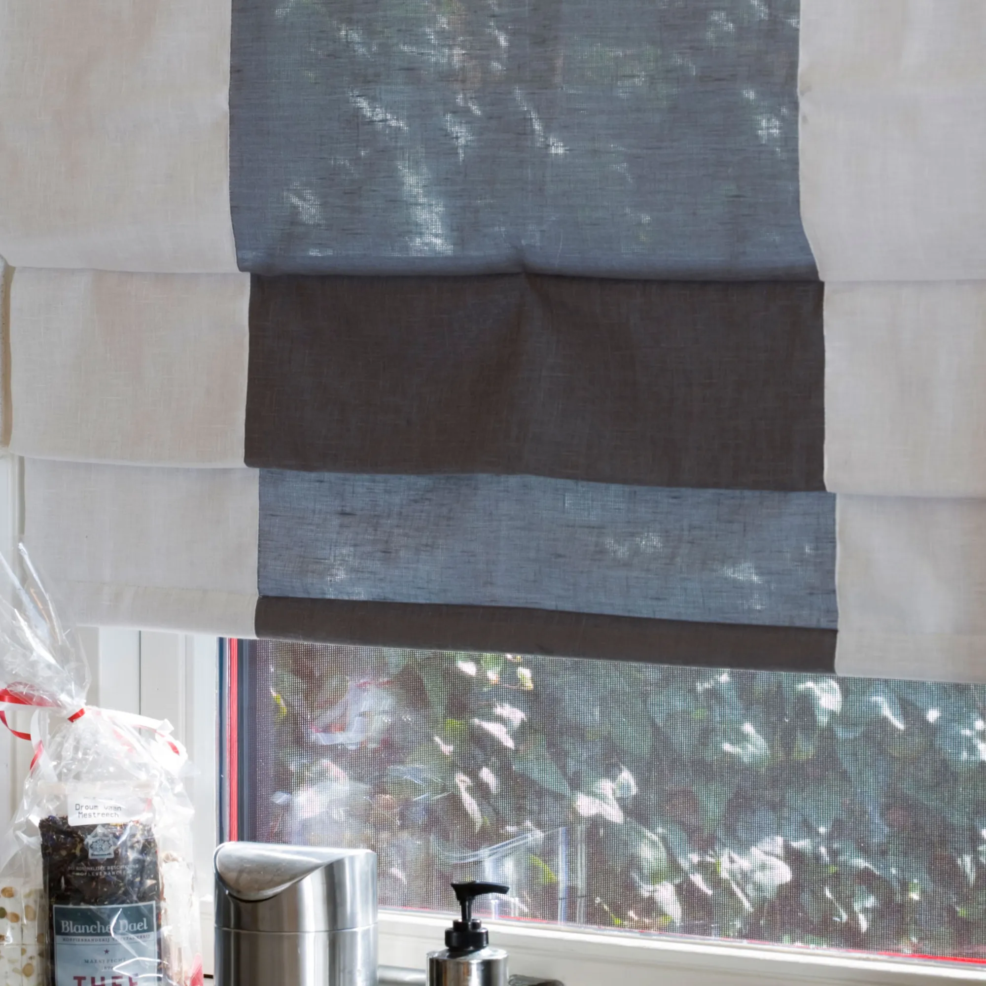 Brooklyn sheer curtain fabric used as a Roman blind, made from 50% polyester and 50% cotton, featuring an inbetween transparent weave with soft horizontal bands that gently filter natural light in a modern interior.