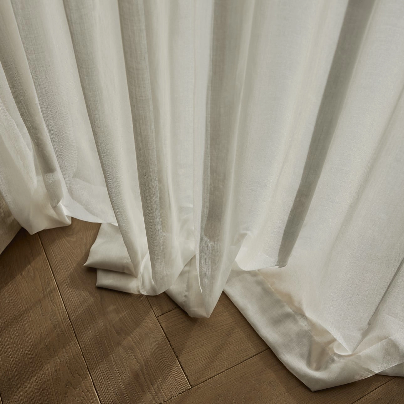 Melbourne sheer curtain fabric with inbetween transparent structure, made from recycled flame-retardant polyester, shown as soft white floor-length drapery pooling gently on wooden flooring, suitable for Roman blinds.