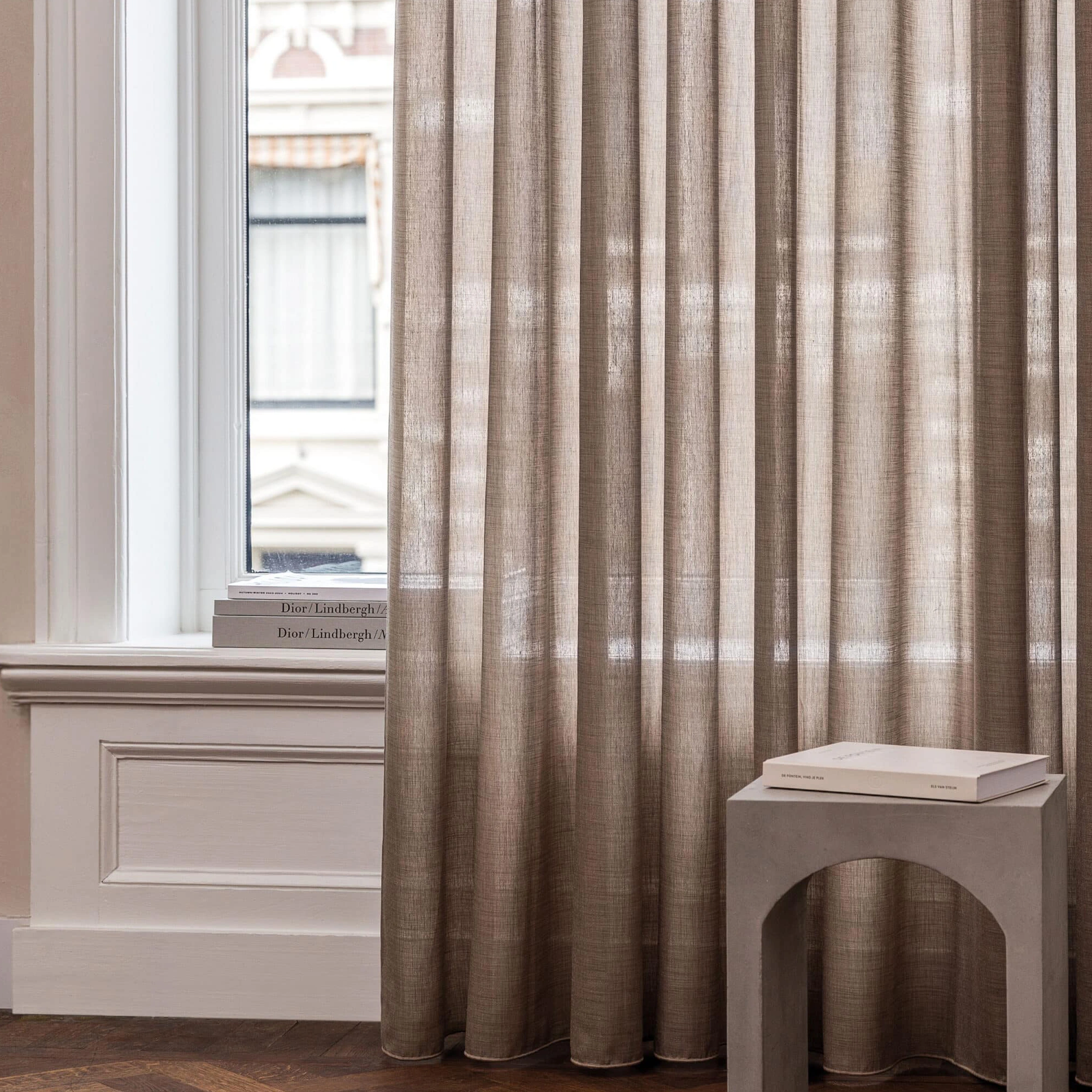 Noa-recycle sheer curtain fabric made from polyester and recycled polyester, shown as inbetween transparent floor-length curtains in a refined modern interior with tall windows, soft neutral tones, and gentle daylight filtering through, OEKOTEX certified.