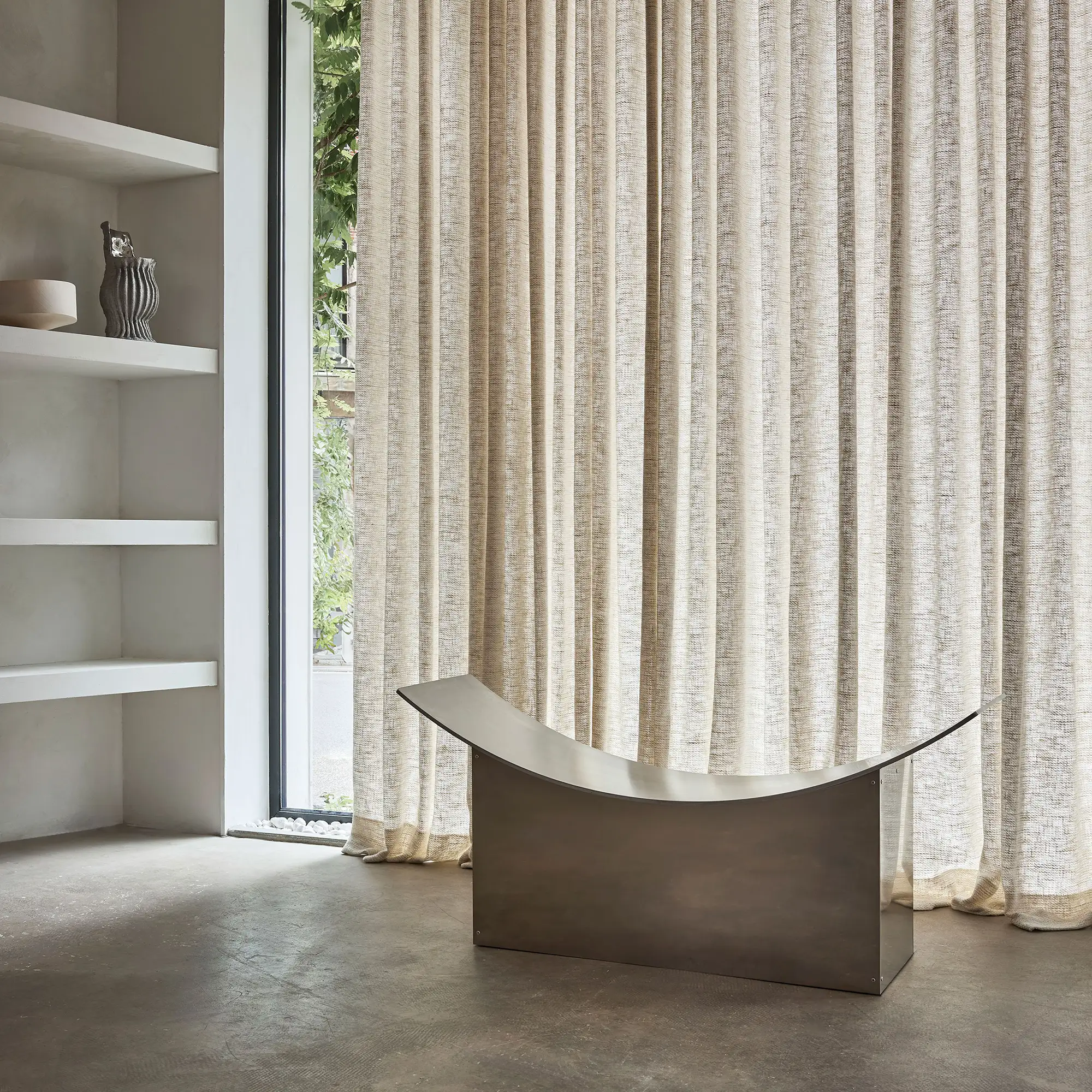 Sonora curtain fabric with an inbetween transparent weave, made from a natural blend of cotton, polyester, linen, and wool, shown as floor-to-ceiling drapery in a minimalist modern interior with built-in shelving, sculptural seating, concrete flooring, and soft natural daylight, OEKOTEX certified.